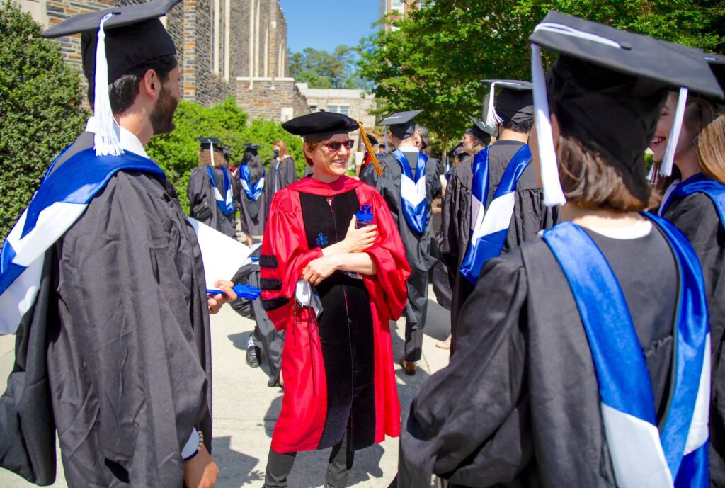 Dean Kelley outside, graduation robes, talking with two graduating students.