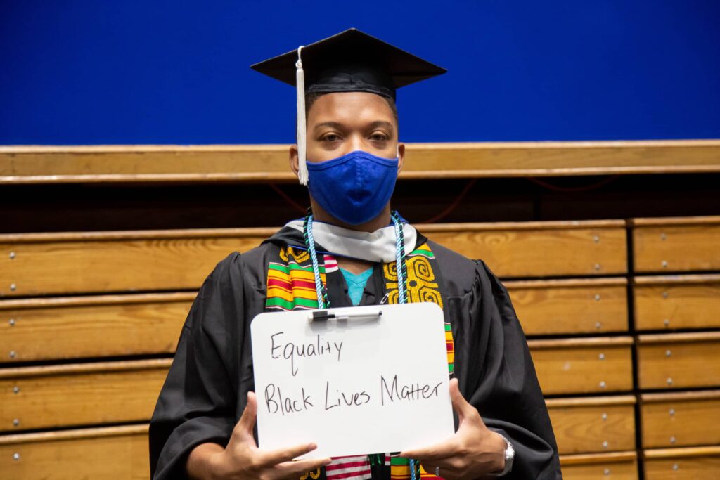 African American man in graduation robes holding Black Lives Matter sign